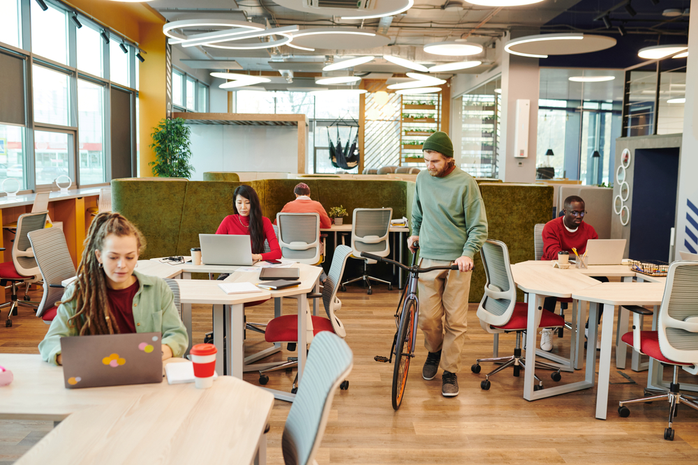 What is office hoteling? And is it similar to hot desking? Modern workspace with people and laptops.