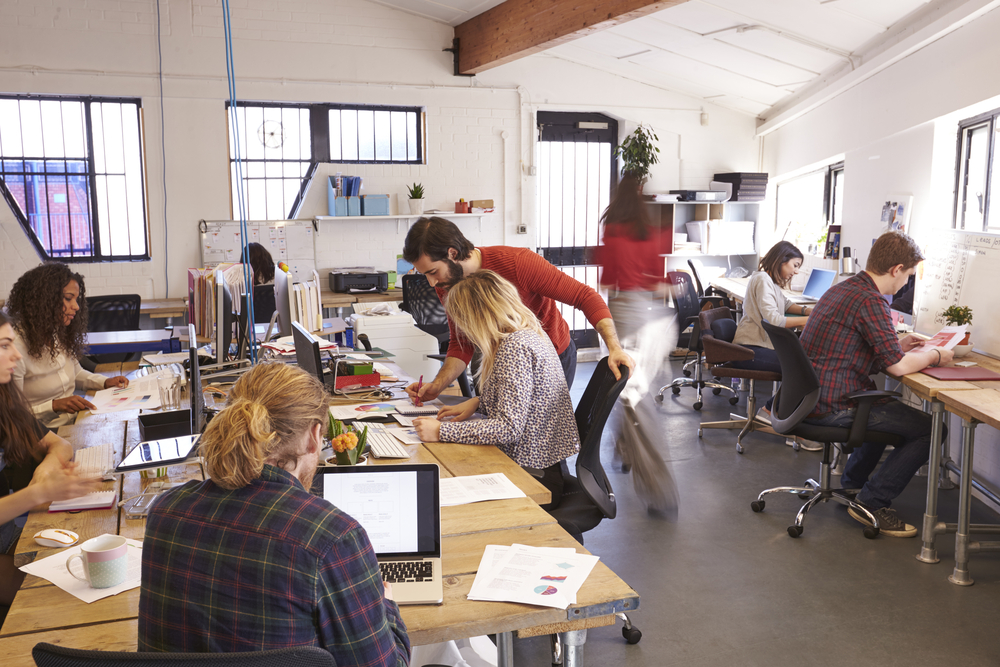 What is office hoteling? And is it similar to hot desking? Busy office with collaborative workspace activities.