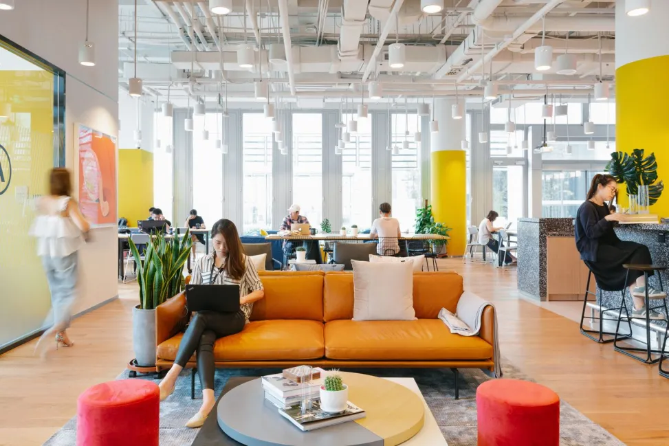 Nine benefits of coworking spaces a woman sitting on a couch in a room with a coffee table and people
